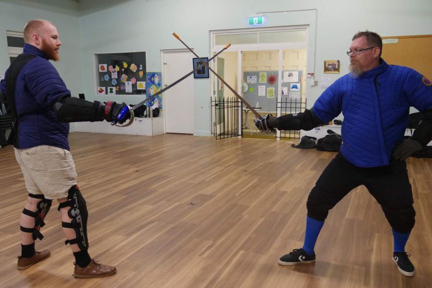 Two men lock their swords together in a church hall