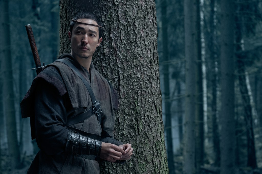 Lan (Daniel Henney) stands in the woods with a sword in "The Wheel of Time." 
