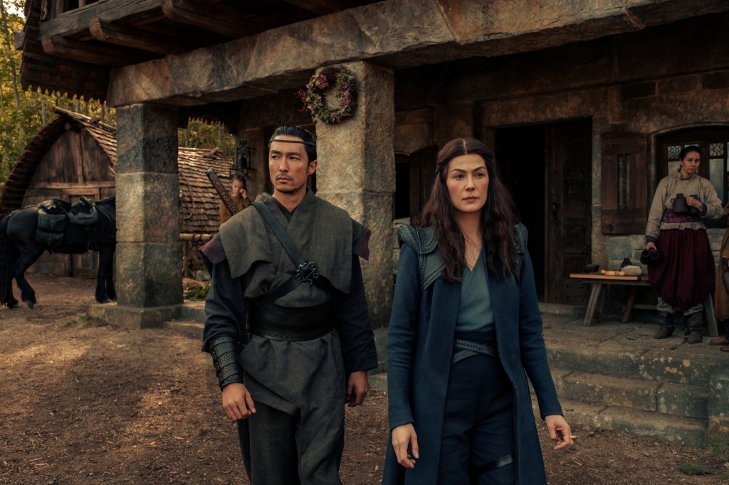 Lan (Daniel Henney) and Moiraine (Rosamund Pike) stroll through the village in "Wheel of Time." 