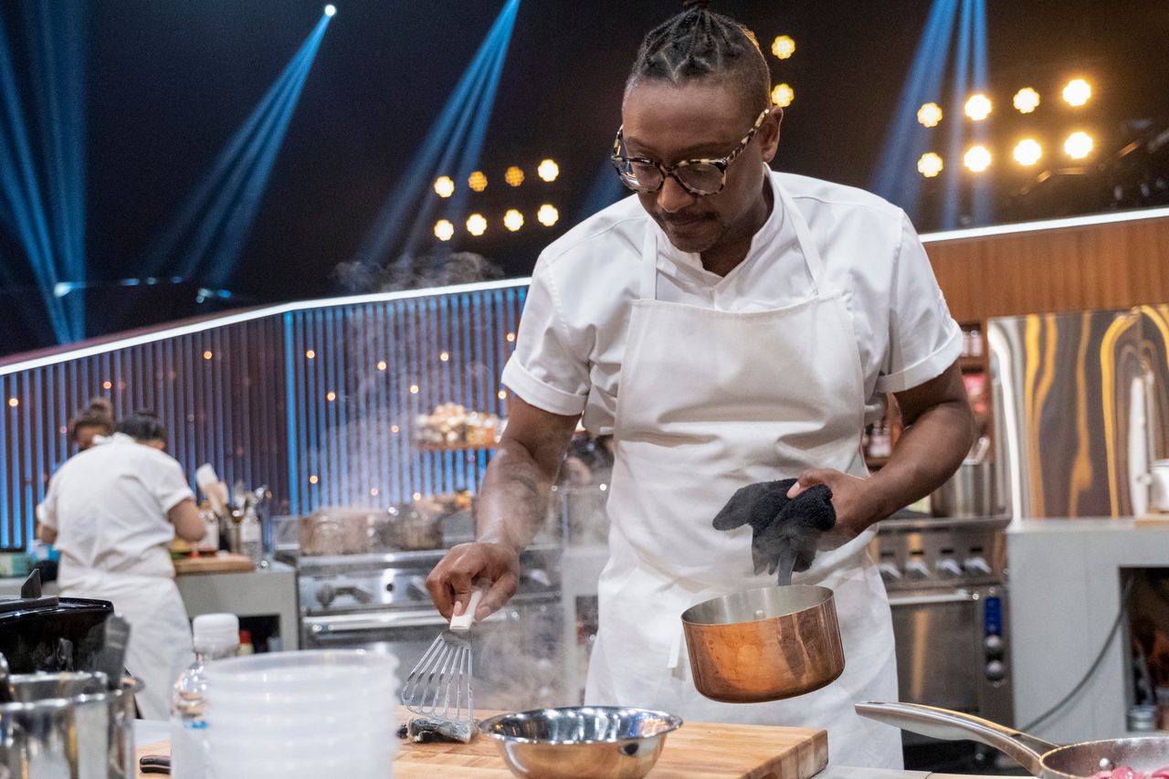 Chef Gregory Gourdet stands in the Kitchen Stadium working on a dish in Iron Chef Quest for an Iron Legend